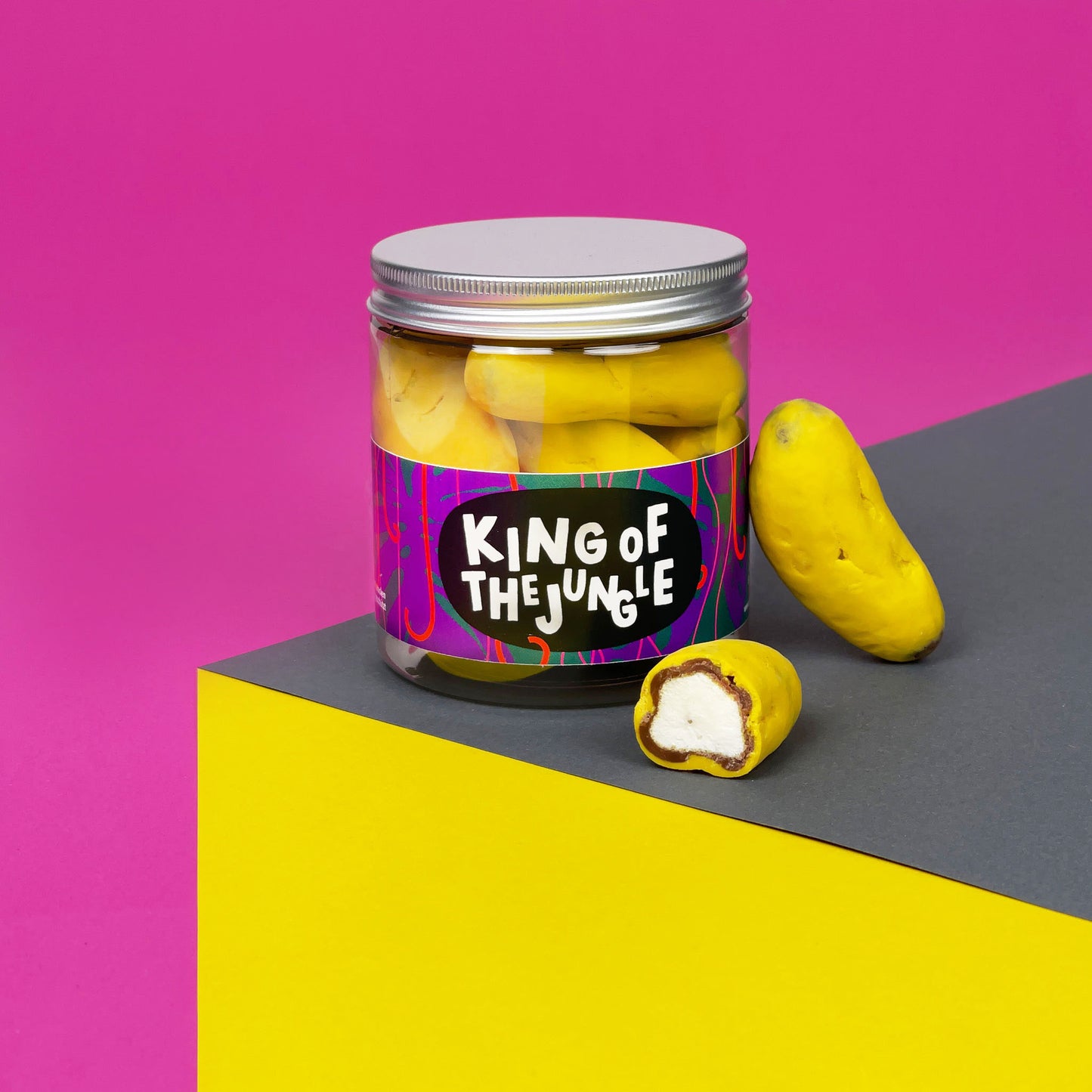 Dose mit Schokobananen vor pinkem Hintergrund. Schaumzuckerbananen mit Vollmilchschokolade umhüllt. Grüße an Haribo.
