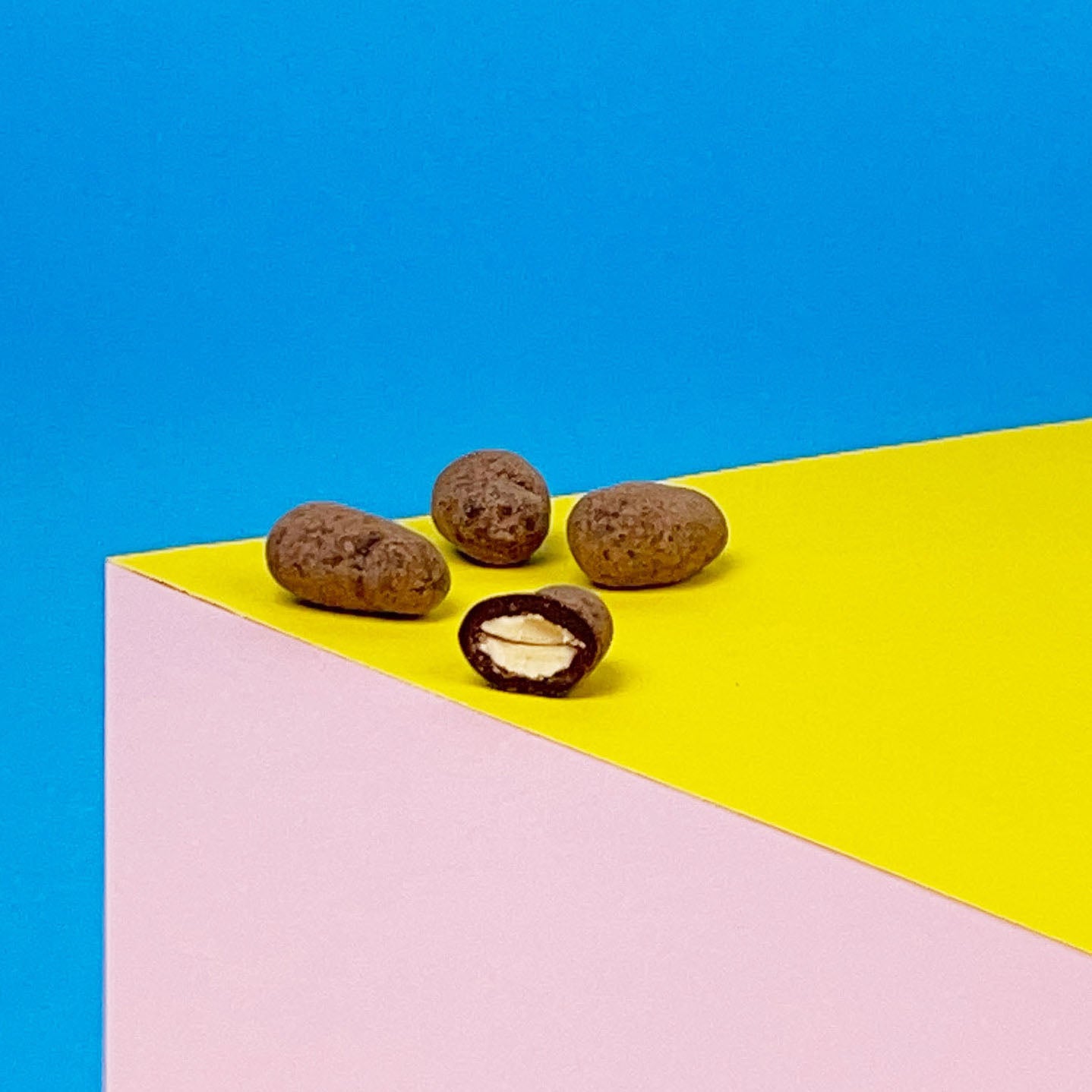 Karamellisierte Mandeln umhüllt von Zartbitterschokolade liegen angeschnitten auf einem bunten Hintergrund. Vegane Schokoladendragees mit außergewöhnlichem Geschmack,