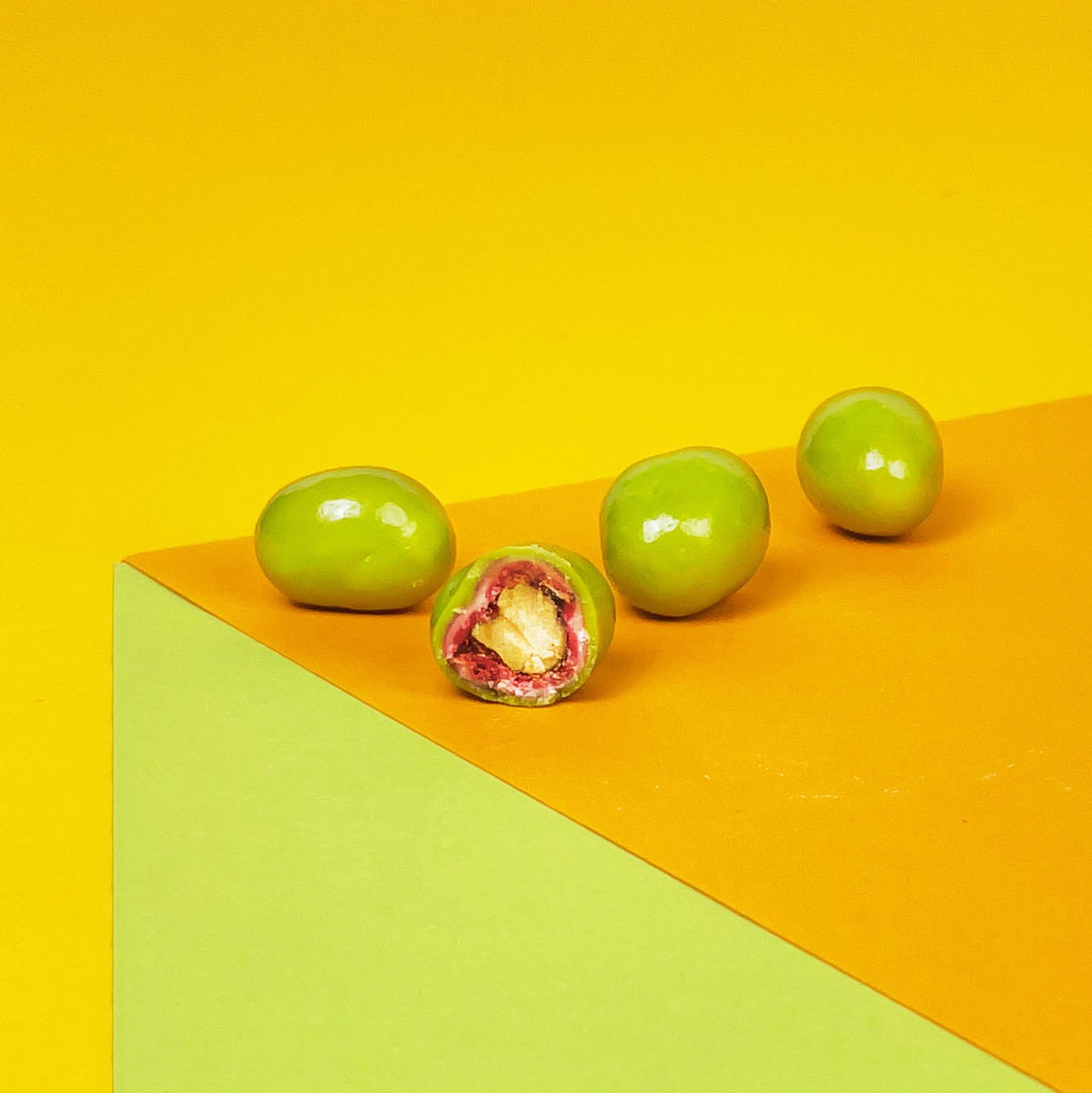 Angeschnittenes Pistaziendragee glänz vor einem gelben Hintergrund. Weiße Schokolade umhüllt die edlen Nüsse.