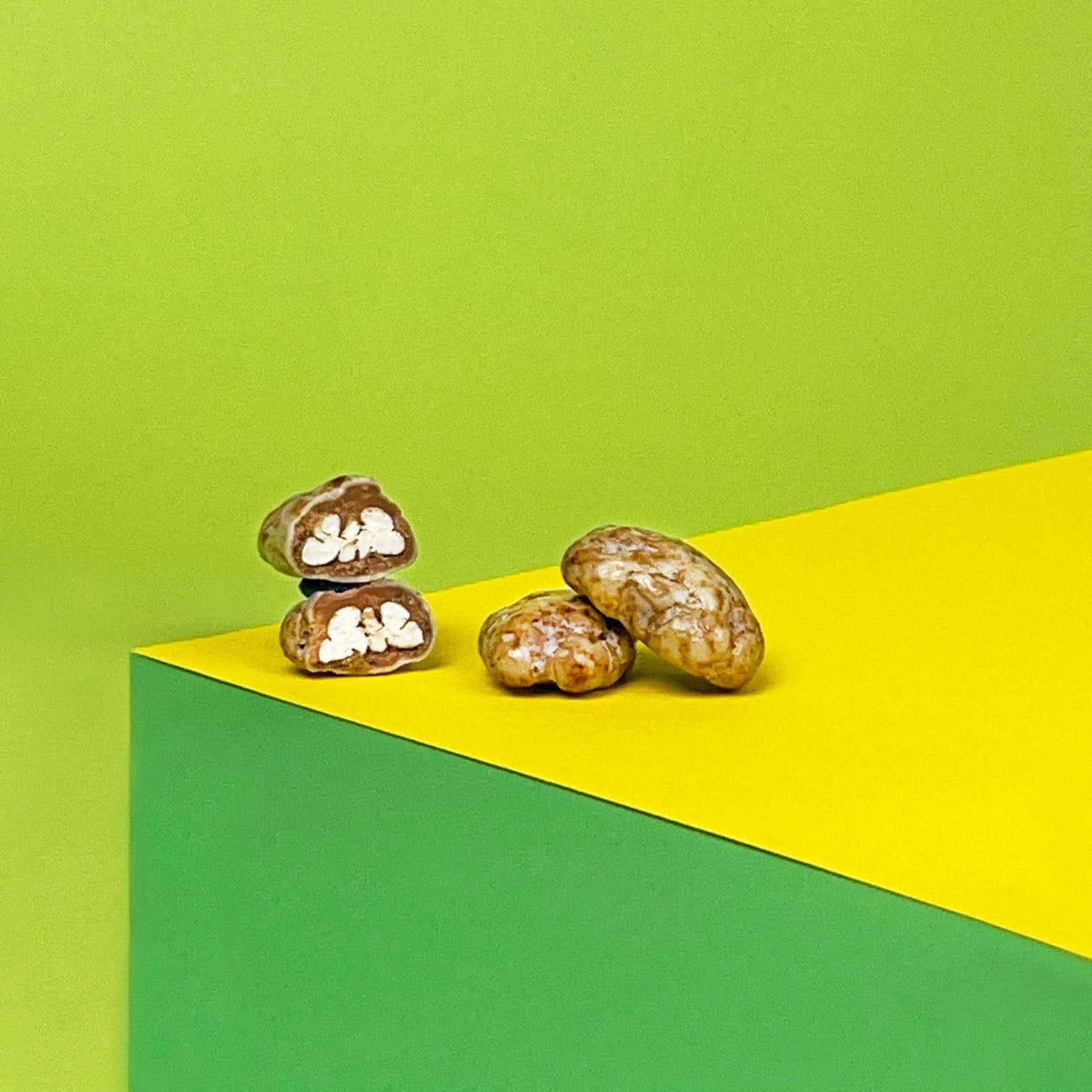 Angeschnittene Pecannuss vor gelbem und grünen Hintergrund. Vollmilchschokolade und weiße Schokolade umhüllen die köstliche Nuss.